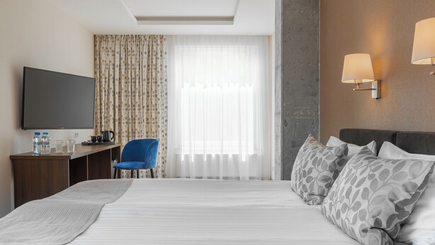 Une chambre d’hôtel comprenant un lit, un bureau avec un téléviseur à écran plat, une chaise, une machine à café et une fenêtre avec des rideaux.