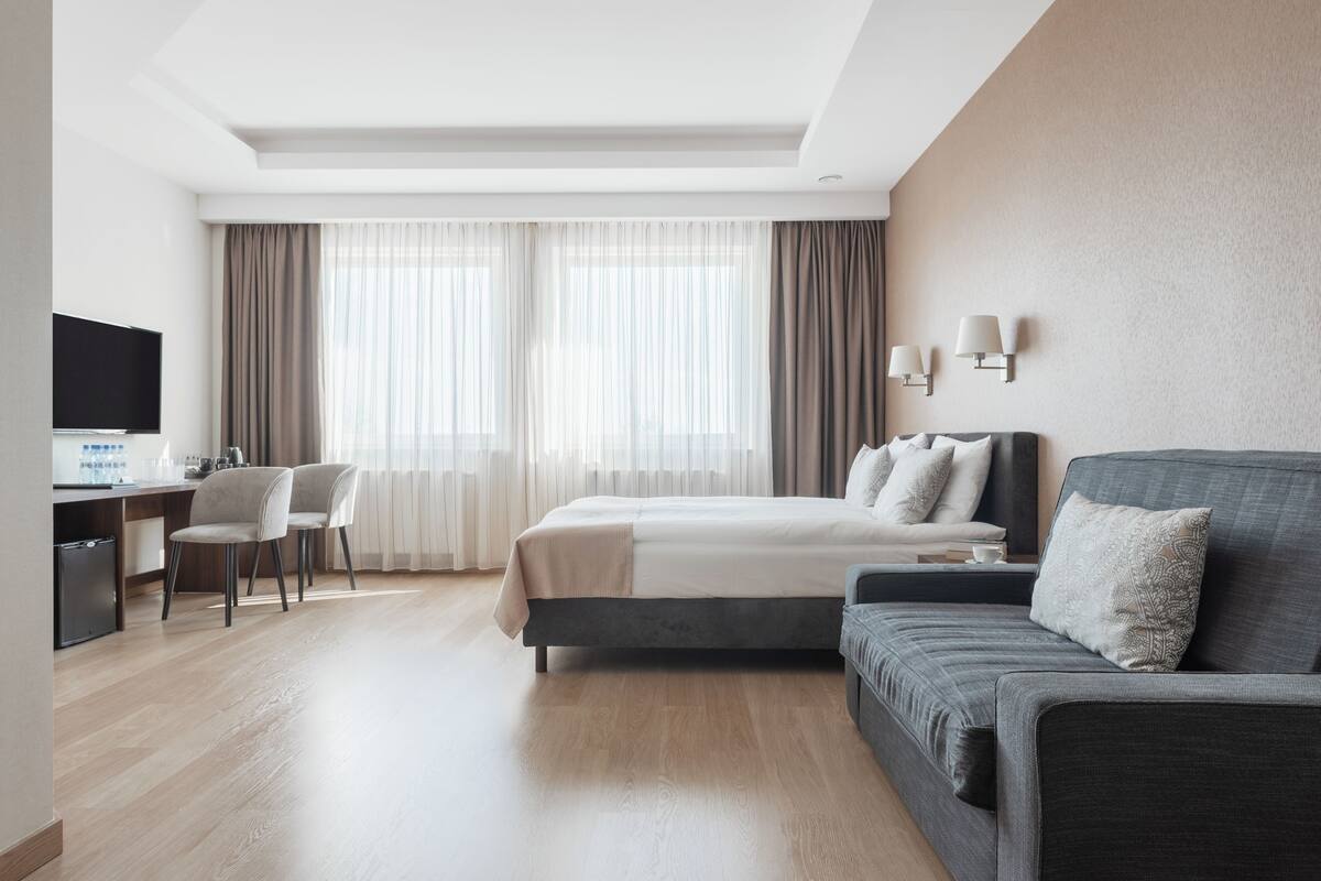 A hotel room with a bed, a desk, a TV, and a sofa.