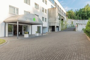 Ein modernes Gebäude mit überdachter Eingangstür, auf der 'green loft' steht, einem gepflasterten Weg und einer Betonkonstruktion mit Bepflanzung.