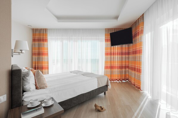 Ein Hotelzimmer mit Bett, Wandfernseher, Nachttisch mit Lampe und Vorhängen.