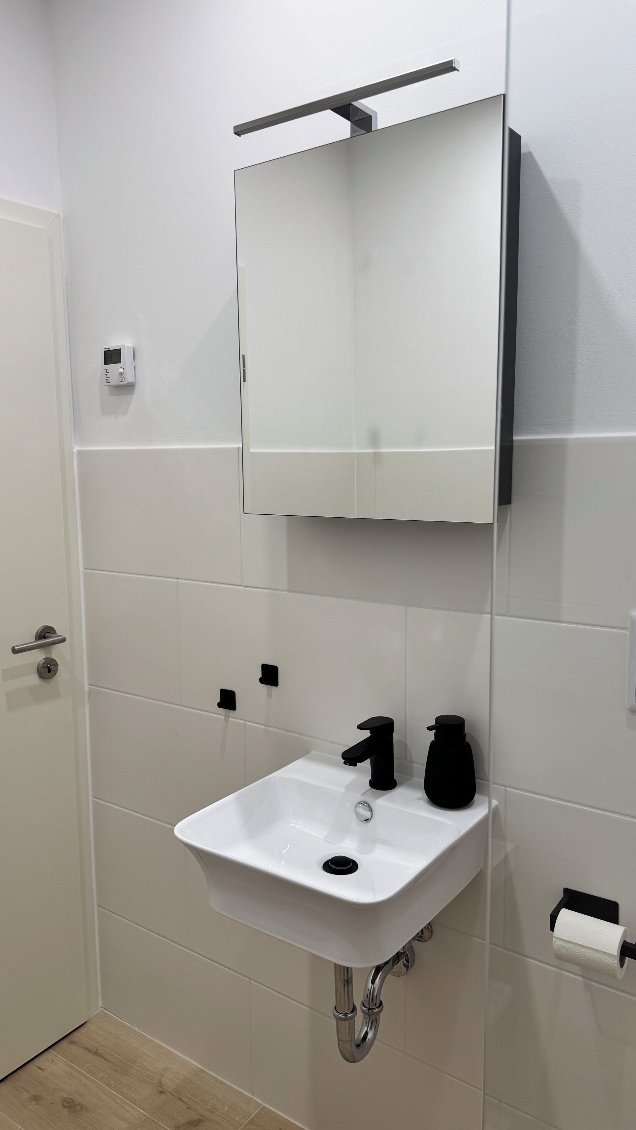 Un baño con un lavamanos blanco, un grifo negro y un espejo encima.