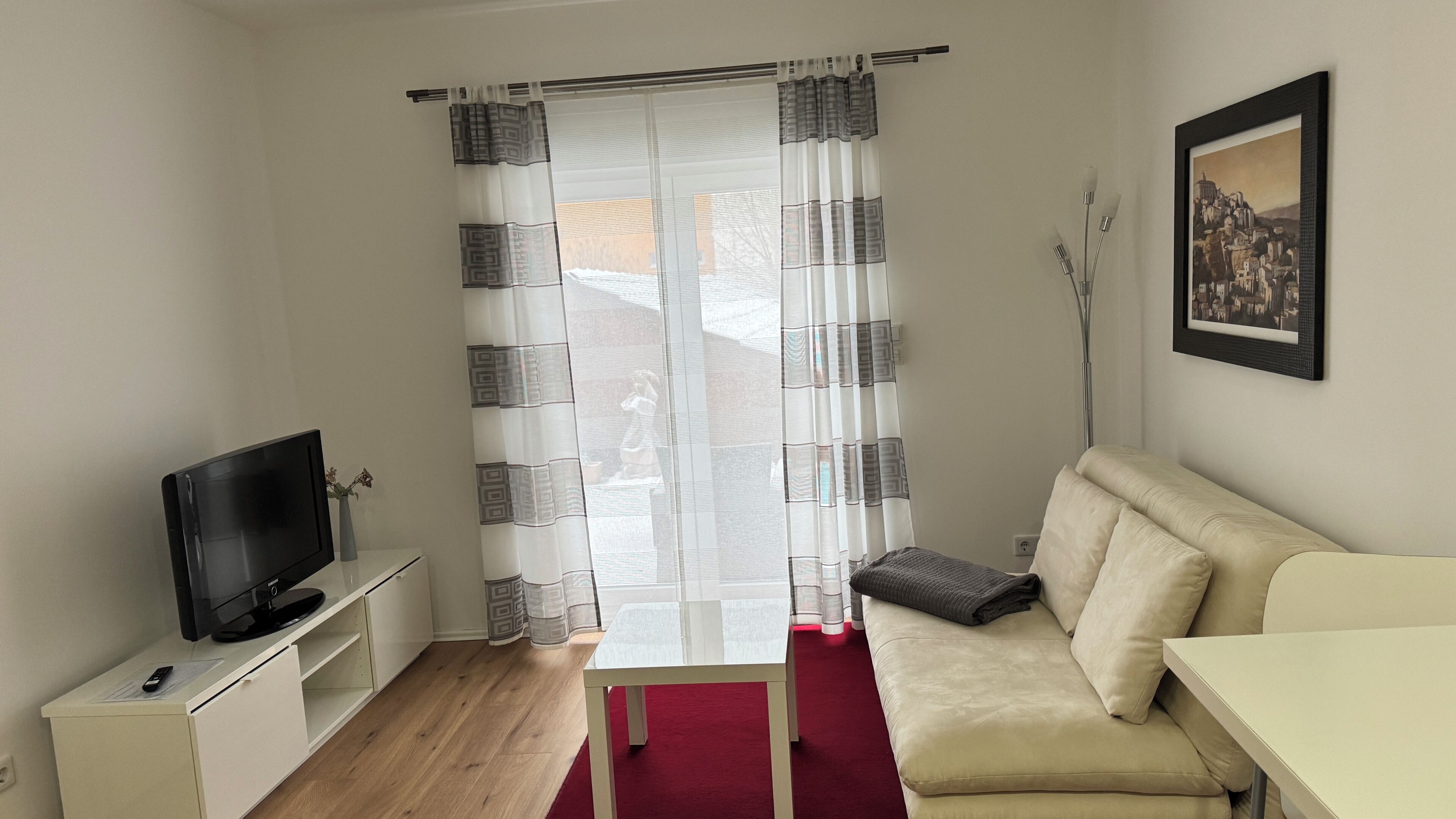 A room with a TV on a stand, a sofa, a small table, and a picture on the wall.