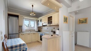 A compact kitchen with a dining area, a refrigerator, a stove, and a window with curtains. - Apartment 'Casa Verde Blu' with Balcony, Wi-Fi and Air Conditioning (Perivoli)