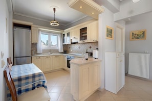 A compact kitchen with a dining area, a refrigerator, a stove, and a window with curtains. - Apartment 'Casa Verde Blu' with Balcony, Wi-Fi and Air Conditioning (Perivoli)
