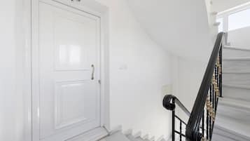 A white door with a brass handle, a black handrail, and a white wall with a light switch.
