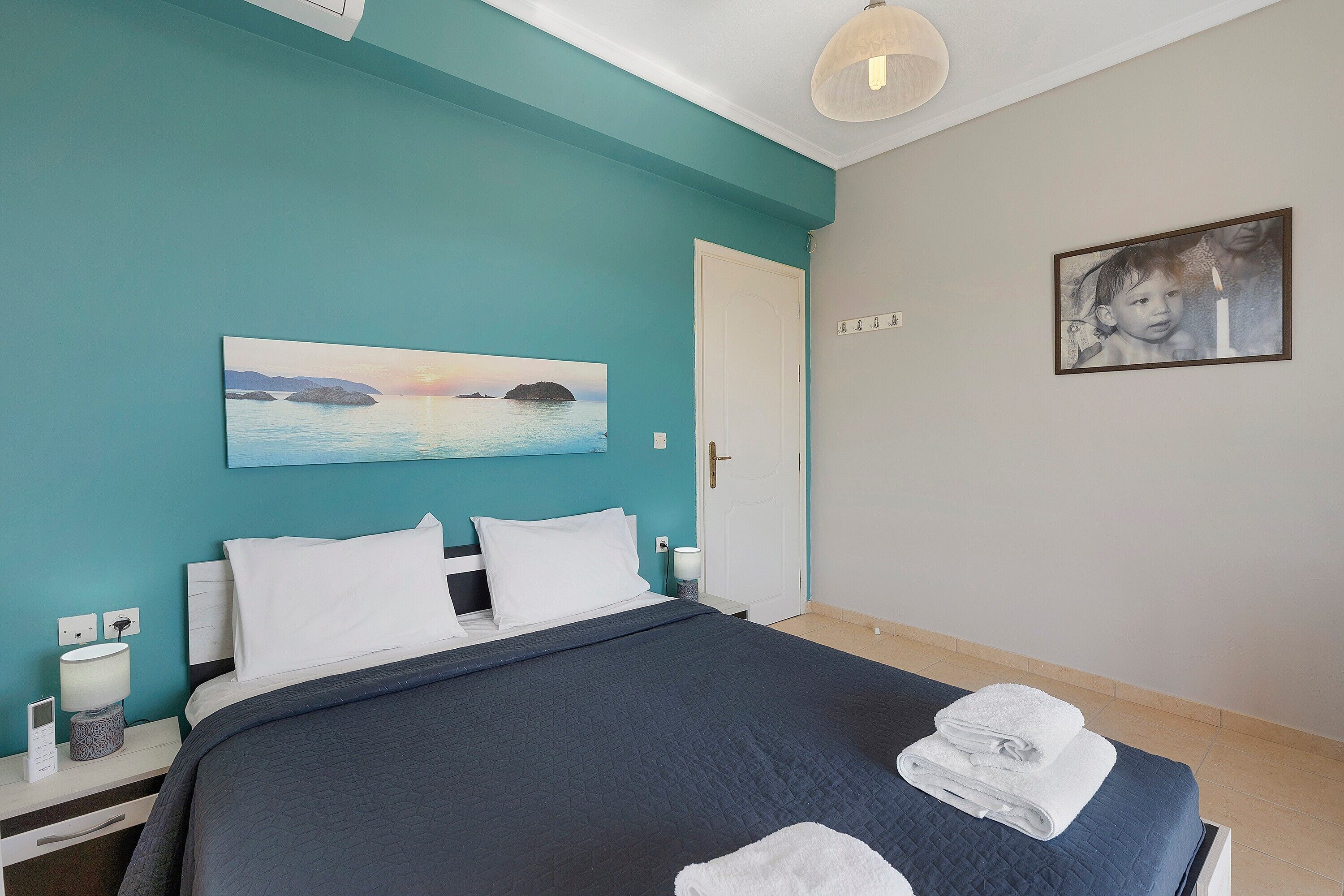 A bedroom with a bed, a nightstand, a lamp, a painting, and a framed photo on the wall.