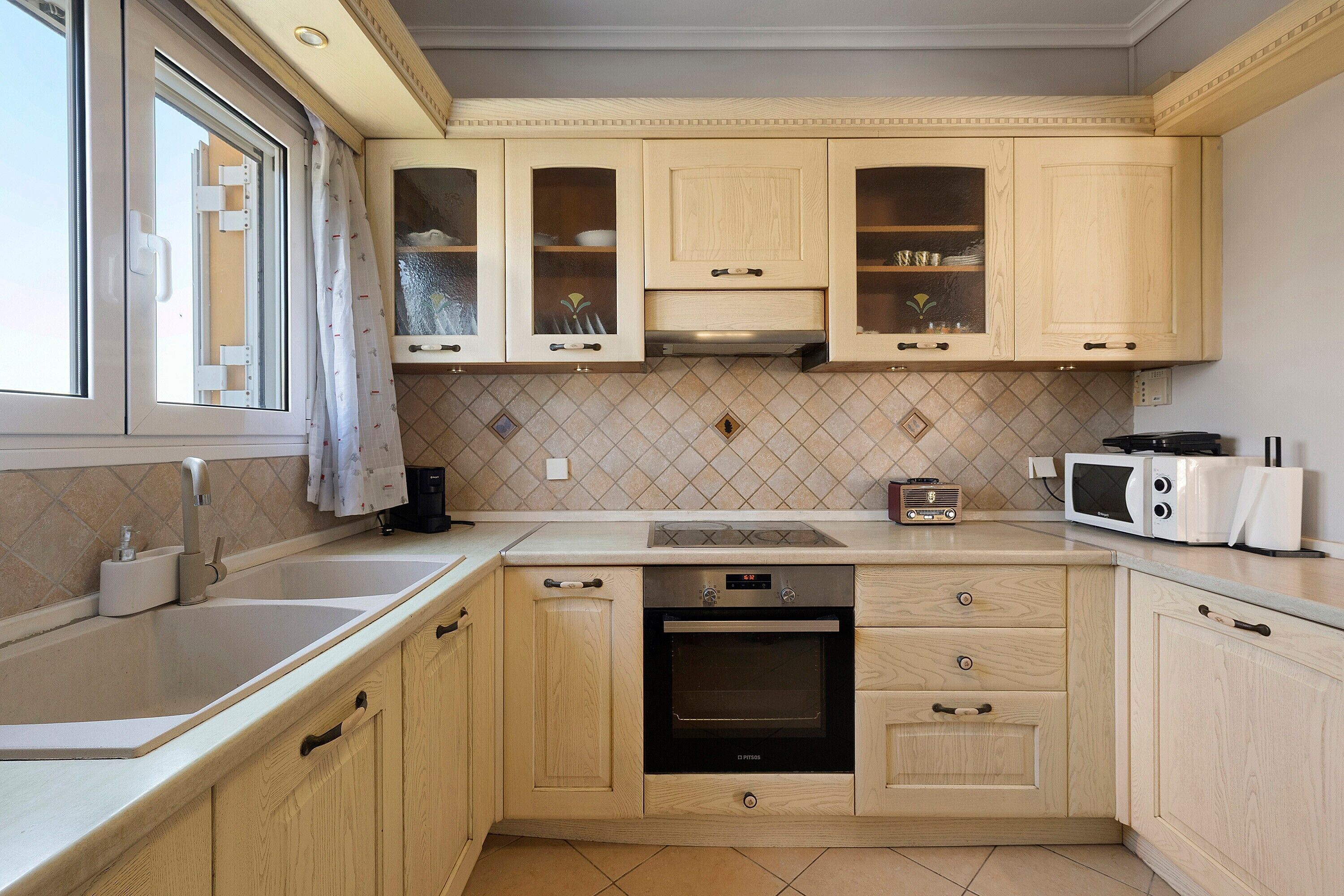 A kitchen with wooden cabinets, a built-in oven, a microwave, and a window with curtains.