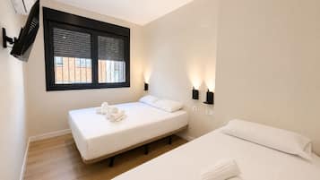 A hotel room with two beds, a TV mounted on the wall, and a window with blinds.