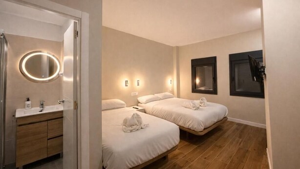 Habitación de hotel con dos camas, baño con espejo e iluminación empotrada.