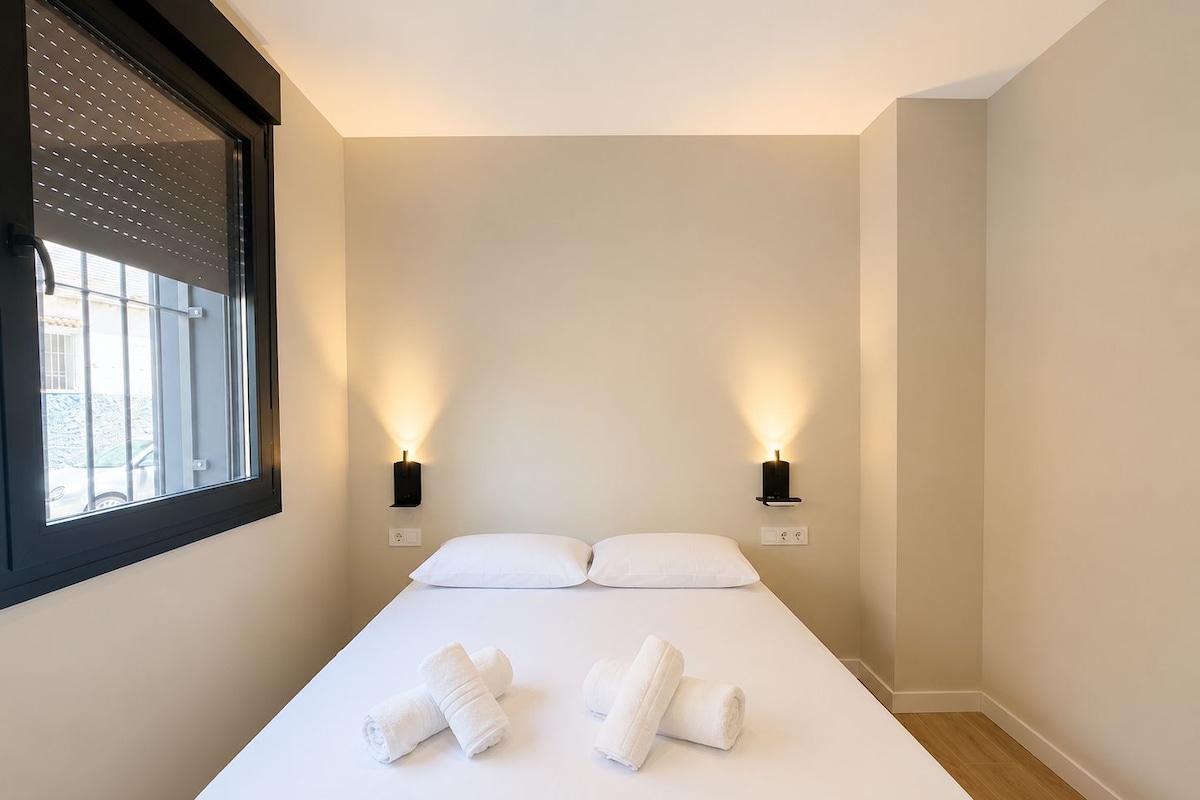 Habitación de hotel con una cama, dos lámparas de pared y un ventanal con persianas.