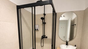 Un baño moderno con ducha de vidrio, lavamanos blanco, espejo e inodoro.