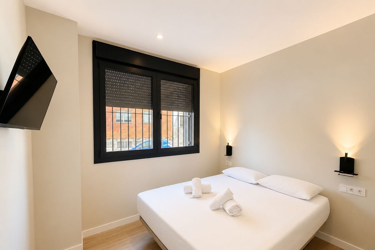 A modern hotel room with a bed, two bedside lamps, a TV mounted on the wall, and a window with blinds.