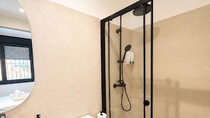 Un baño moderno con cabina de ducha de vidrio, inodoro blanco, lavamanos y espejo.