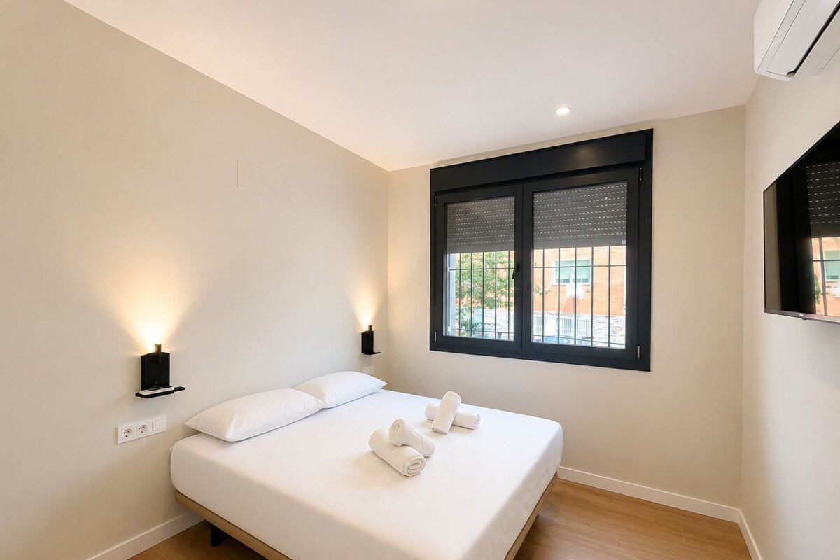 Quarto de hotel com cama, duas luminárias fixadas na parede, janela com persianas e ar condicionado.