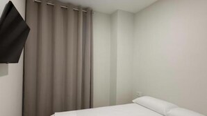 Una habitación de hotel con cama, cortinas, televisión de pantalla plana y una lámpara en el techo.