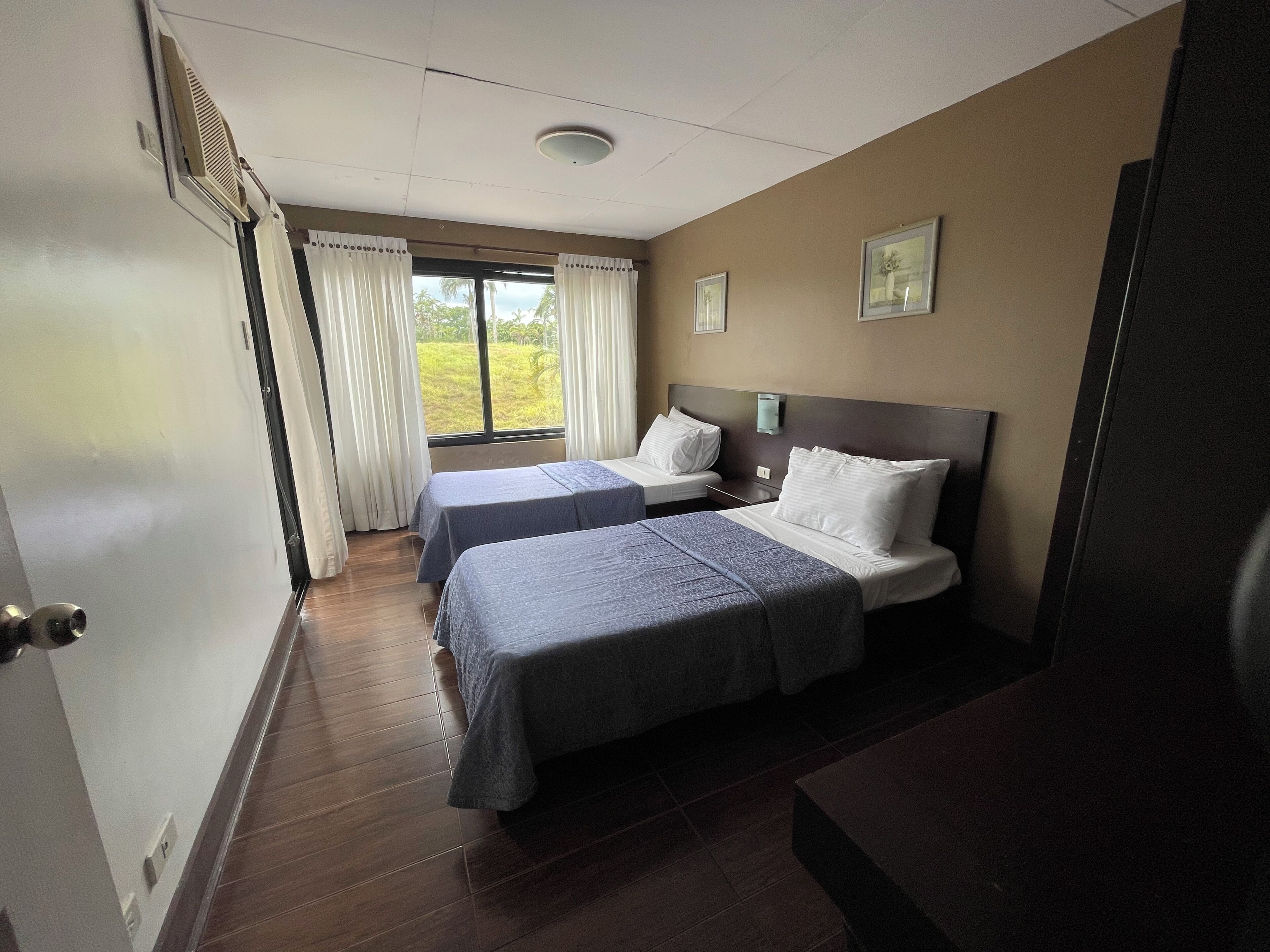 Une chambre d’hôtel avec deux lits, une fenêtre avec des rideaux, une table de chevet et un luminaire fixé au mur.