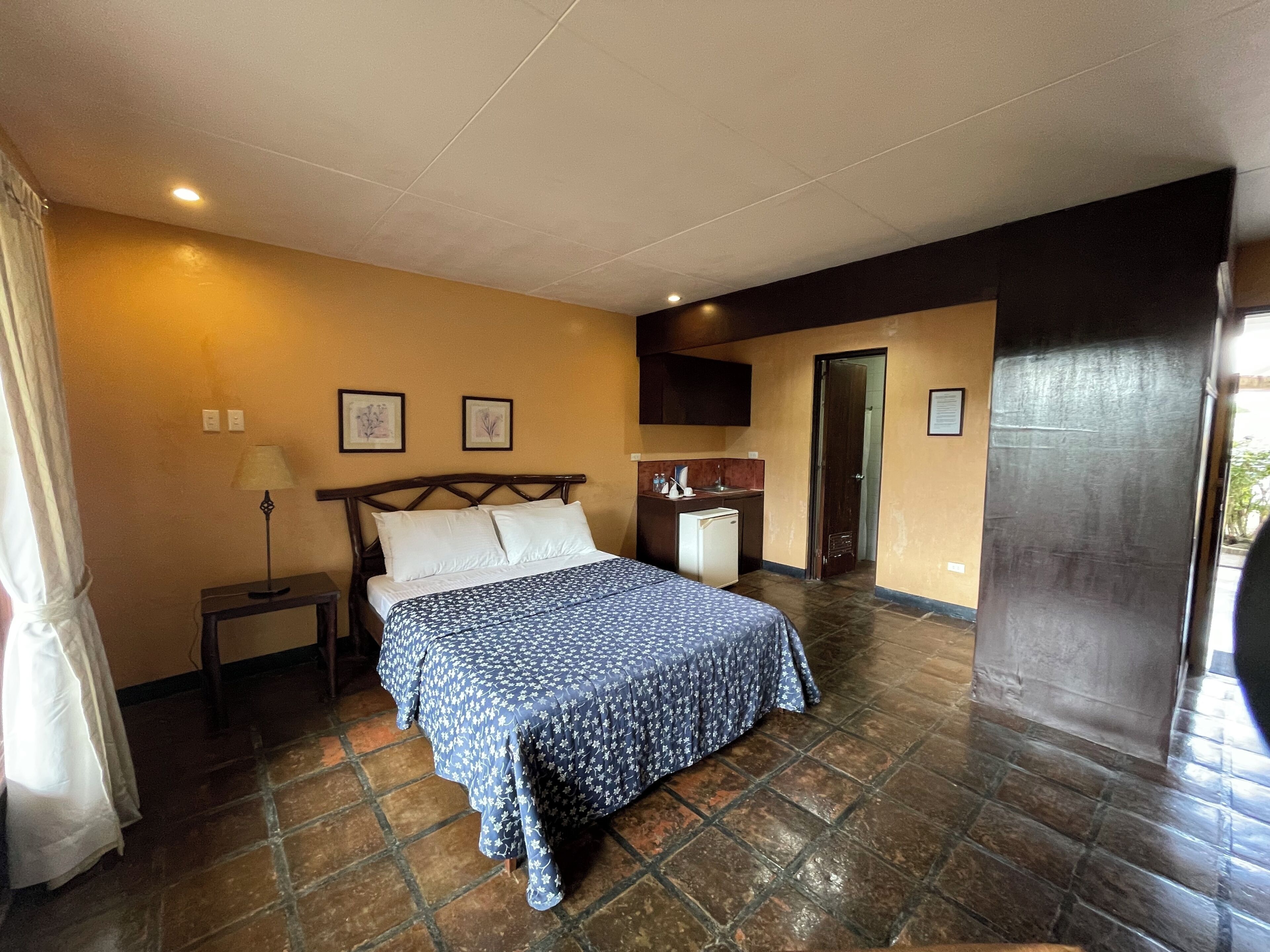 Une chambre avec un lit, une table de chevet, une lampe et une petite kitchenette.