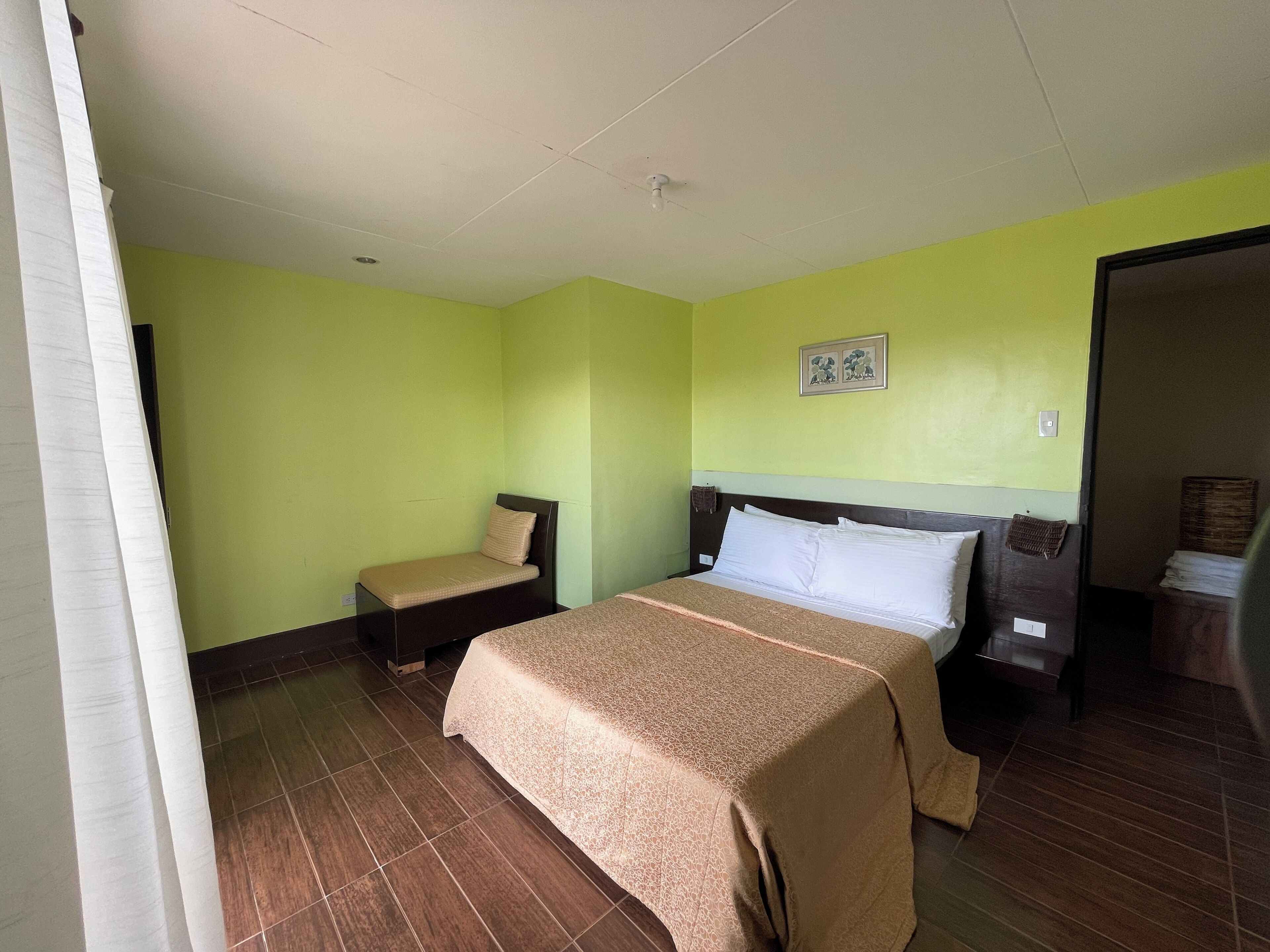 Ein Zimmer mit einem Bett, einer kleinen Bank und einem Wandbild.