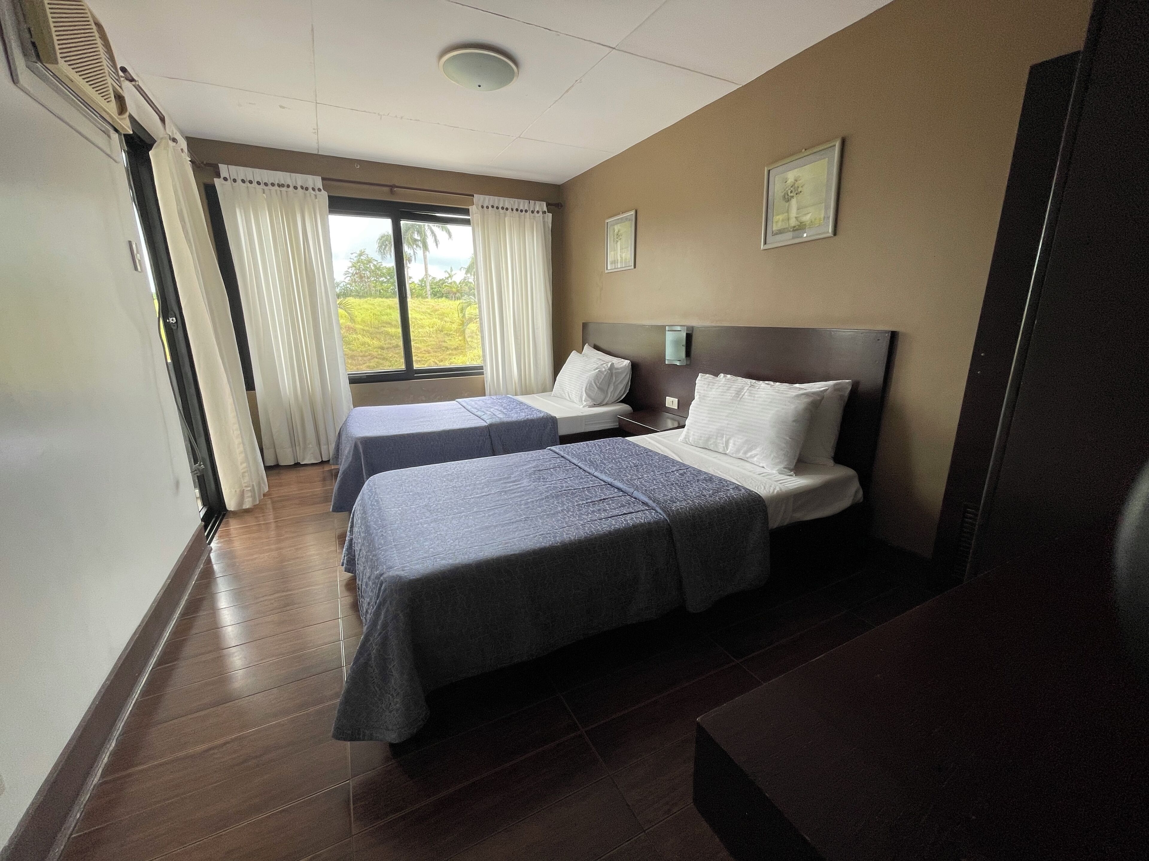 Habitación de hotel con dos camas, un ventanal con cortinas, un televisor de pantalla plana y un respiradero en el techo.