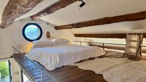 Un dormitorio con techo de madera, un ventanal redondo, una cama con sábanas blancas y una alfombra de piel.