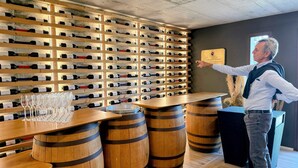 Una bodega con estanterías de madera llenas de botellas de vino, barriles de madera y una zona de bar con copas.