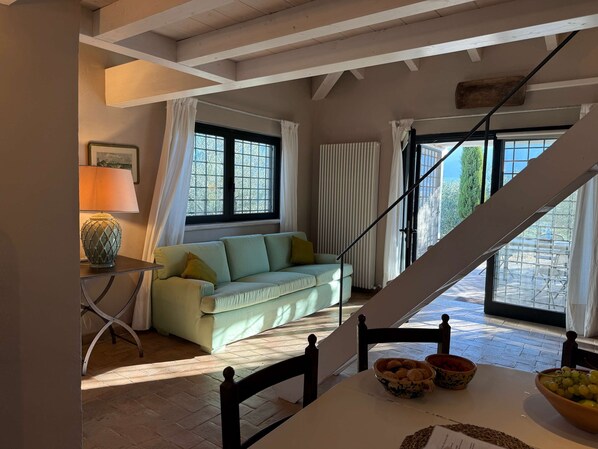 Ein Zimmer mit einer Couch, einem Tisch mit Fruchtschalen, einer Lampe und einem Fenster mit Vorhängen.