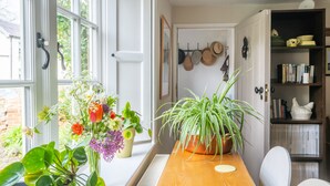 A dining area with a wooden table, potted plants, and a window with a view of greenery.