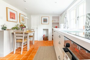 Una cocina moderna con armarios blancos, una zona de comedor con una mesa y sillas de madera, y un ventanal que proporciona luz natural.