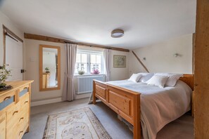 Un dormitorio con cama de madera, cómoda, ventana con cortinas, radiador y espejo.