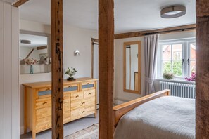 A bedroom with a wooden bed, a dresser, a mirror, and a window with curtains. - 8 Cross Street, Hoxne, Suffolk (Hoxne)