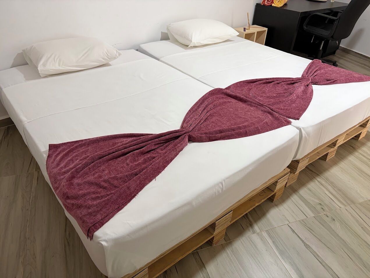 Ein Doppelbett mit weißer Bettwäsche und einem bordeauxroten Handtuch, das zu einem Bogen gebunden ist.