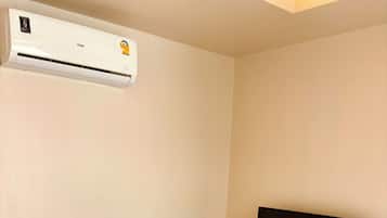 Una habitación de hotel con una cama, un televisor sobre un soporte de madera y un equipo de aire acondicionado en la pared.