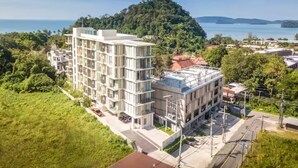 A multi-story building with balconies, surrounded by greenery and a view of the sea. - Breezy Condo in Aonang (Krabi)