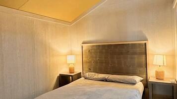 Een eenpersoonsbed in een kamer met een schuine plafond, twee nachtkastjes met lampen, en een airconditioning.