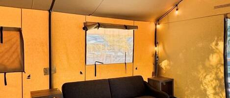 Una habitació acollidora amb un sofà, una taula petita, una finestra amb vista i un projector fixat a la paret.