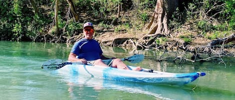 A man in a kayak on a calm river surrounded by dense greenery.