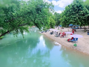 Un cadre agréable au bord de la rivière, avec une plage de sable, des arbres et des espaces de repos en plein air.