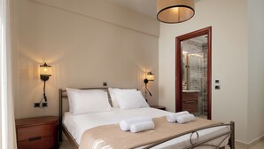 A neatly made bed with white linens and two rolled towels, a wooden nightstand with a drawer, a wall-mounted lamp, and a mirror on the wall. - Casa di Vasia (Gennadi)