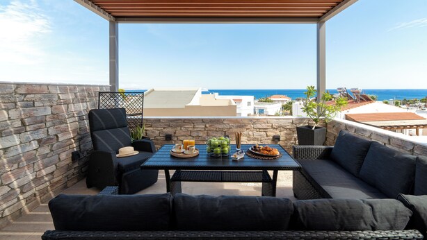A covered outdoor seating area with a stone wall, a table with food and drinks, and a view of the sea. - Casa di Vasia (Gennadi)