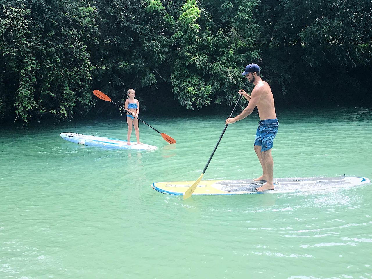 Two people paddleboarding on calm water with dense greenery in the background.