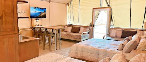 Alojamiento con tienda de campaña, dos camas, zona de comedor, televisor y kitchenette.