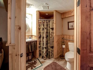 Een houten badkamer met douchegordijn, toilet en wastafel.