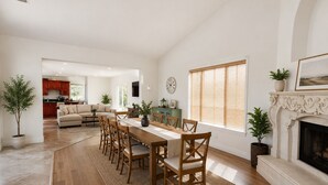 A spacious living area with a dining table, wooden chairs, a fireplace, and a kitchen in the background.