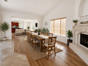 Un salón amplio con una mesa de comedor, sillas de madera, una chimenea y una cocina al fondo.