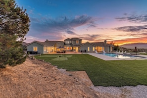 A large house with a swimming pool, a well-maintained lawn, and a view of the sunset.