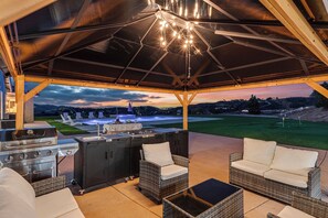 An outdoor patio with a grill, seating, and a view of a swimming pool and landscape.