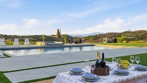 An outdoor dining area with a pool, chairs, and a table set for a meal.
