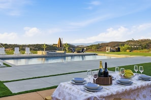 An outdoor dining area with a pool, chairs, and a table set for a meal.