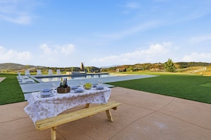 Un área de comedor al aire libre con piscina y vistas a las colinas de fondo.