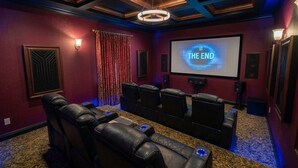 A home theater room with a large screen displaying 'THE END,' leather reclining chairs, a carpeted floor, and a ceiling with a circular light fixture.
